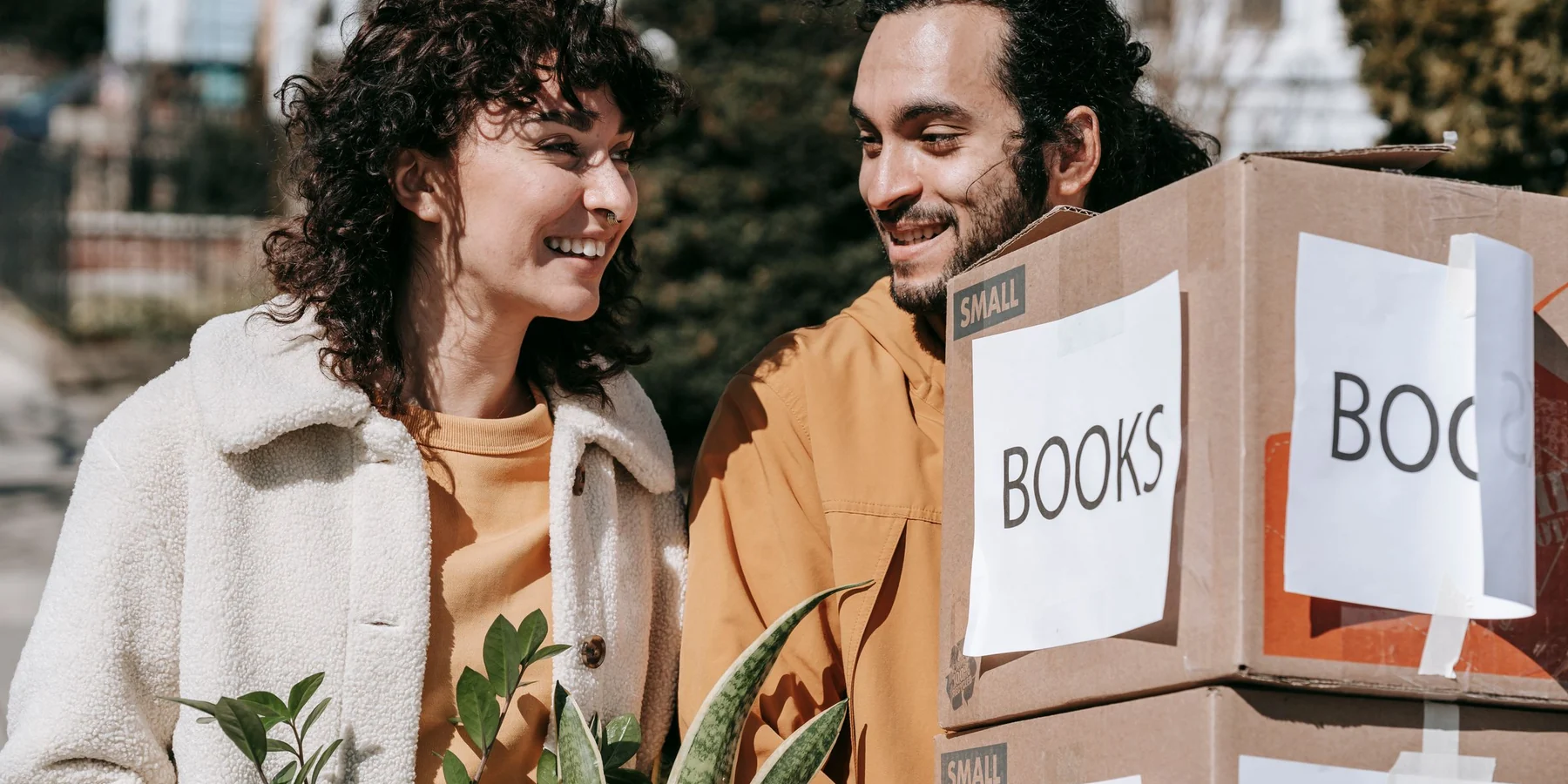 Couple carrying boxes and plants into their new home